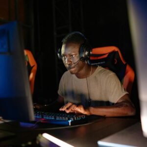 Young adult male intensely focused on computer gaming, using headset and gaming keyboard indoors.